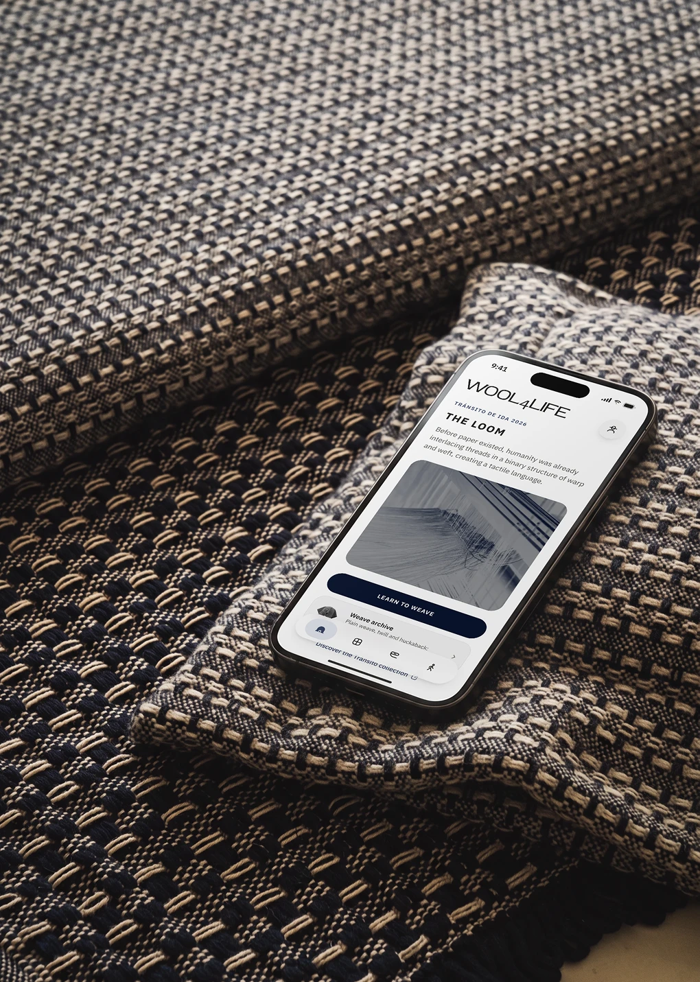 Un iPhone con la pantalla de inicio de Loom sobre un cojín tejido en azul marino y crudo.