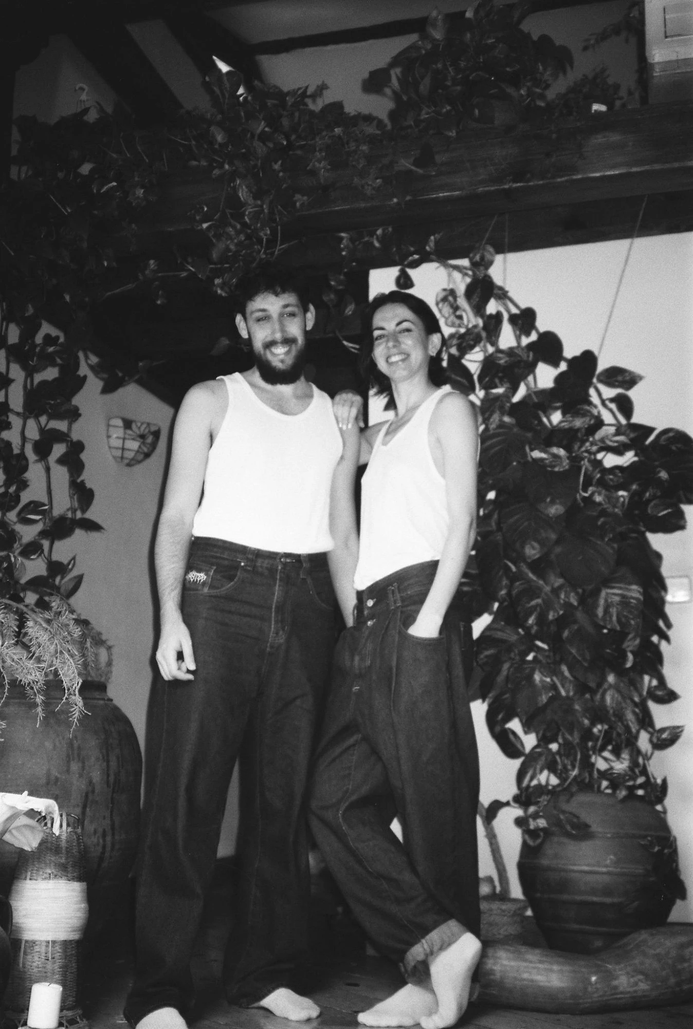 Adriana y Gonzalo, en camiseta blanca y vaqueros, entre plantas y vasijas de barro, en blanco y negro.