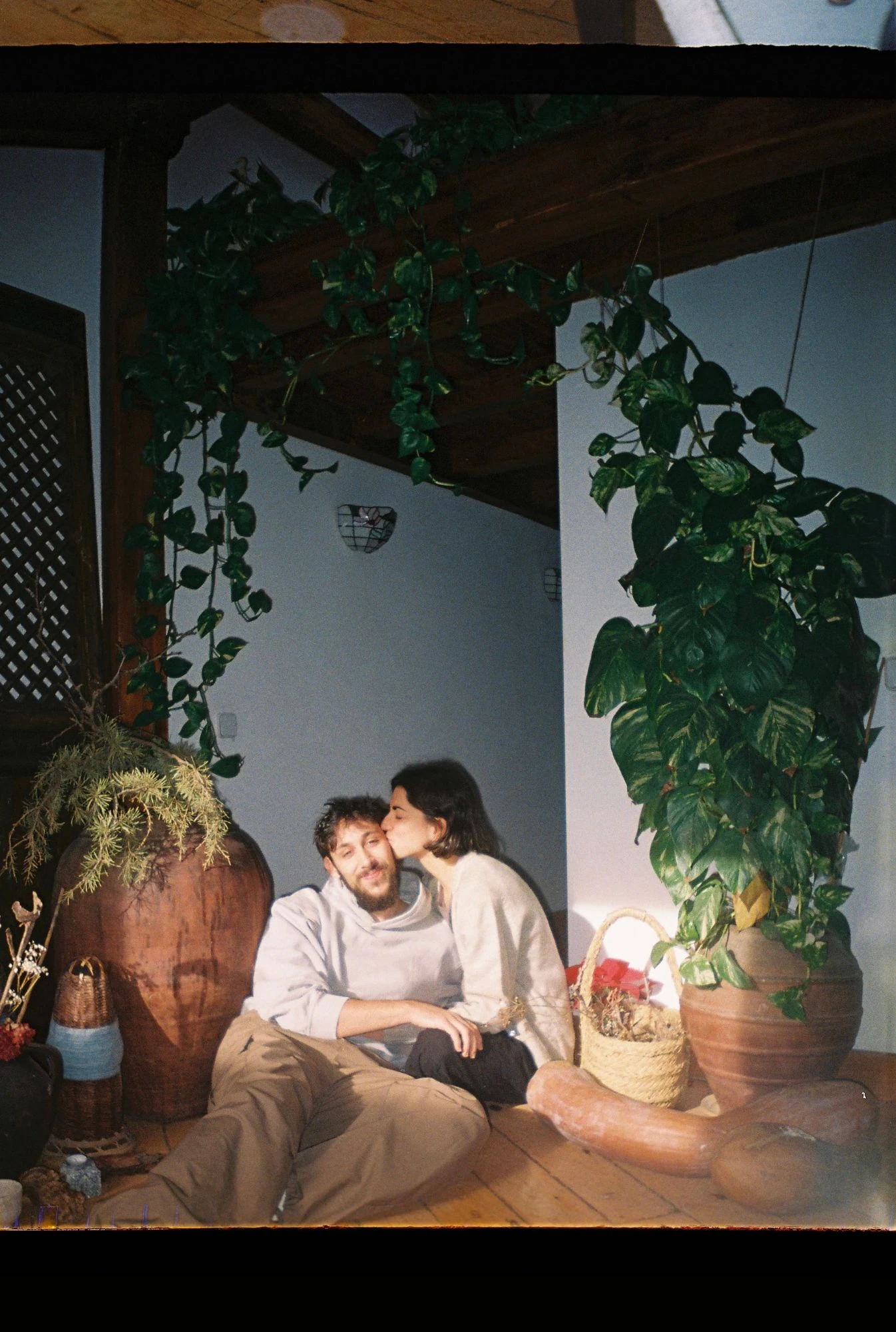 Adriana y Gonzalo sentados en el suelo entre plantas colgantes y vasijas de barro.