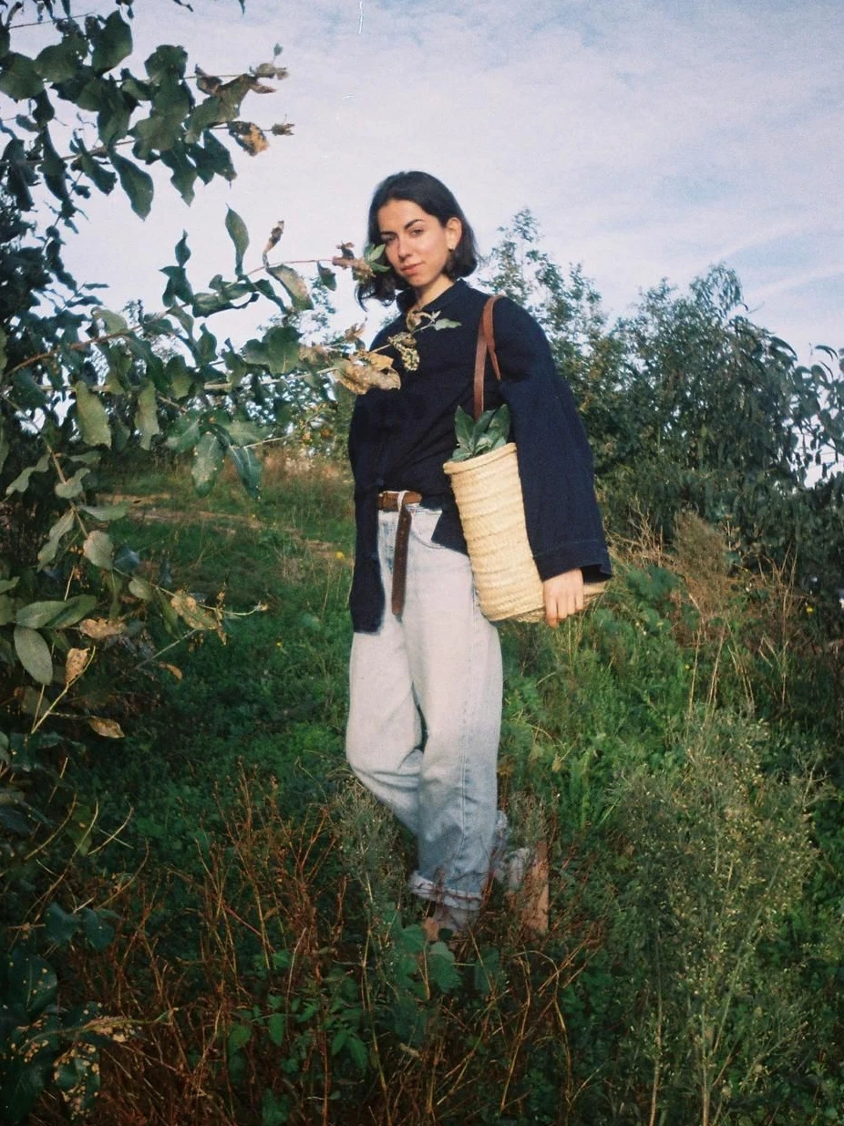 Adriana Cagigas en un campo de hierba alta, con una cesta de mimbre al hombro.