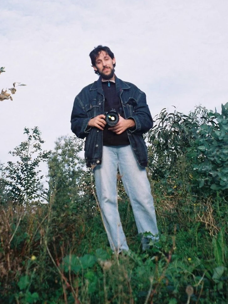 Gonzalo Álvarez en un campo de hierba alta, con una cámara de fotos en las manos.
